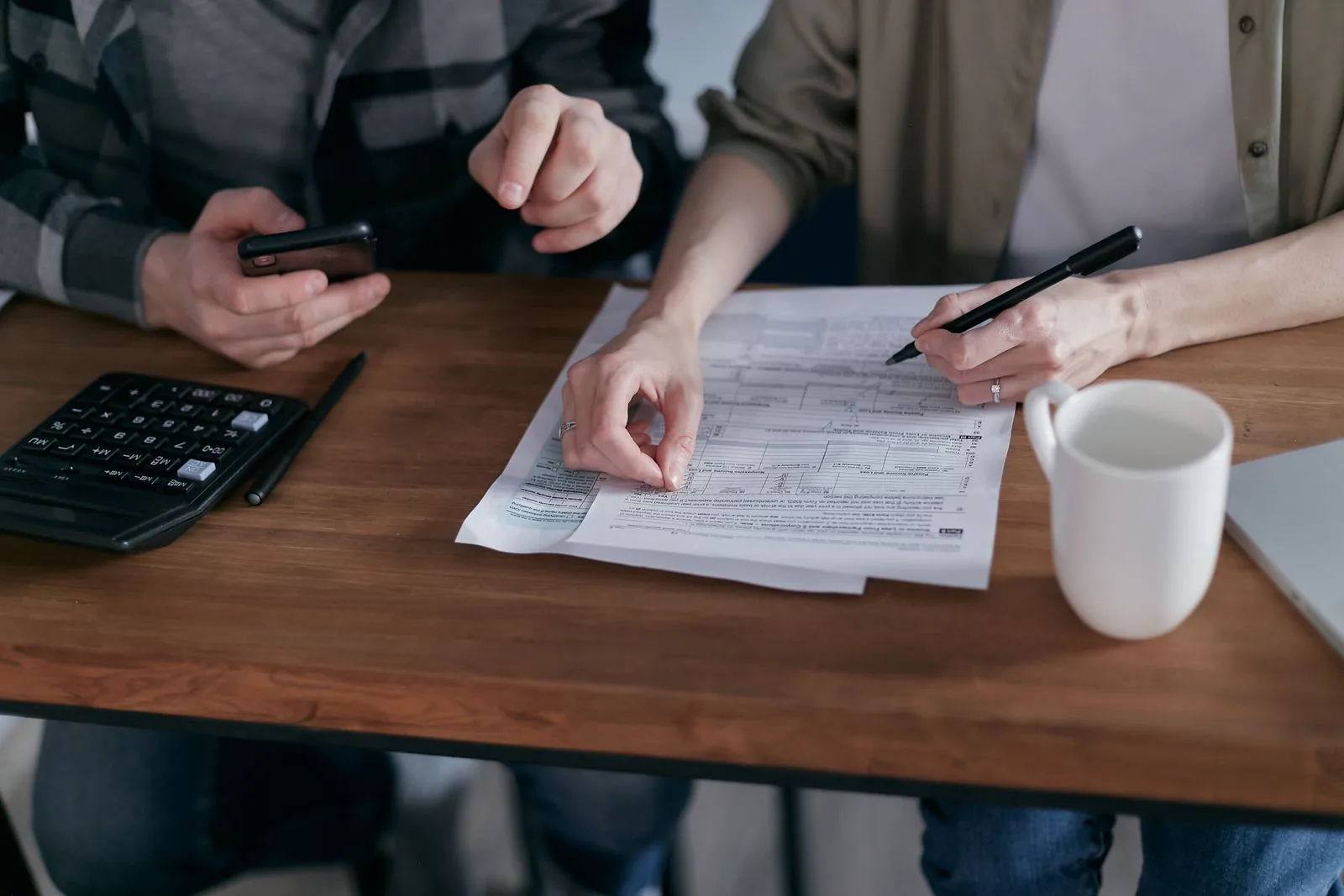 Do you qualify for an FHA loan in Portland, ME Couple at a kitchen table reviewing financial documents with a calculator before applying for an FHA loan