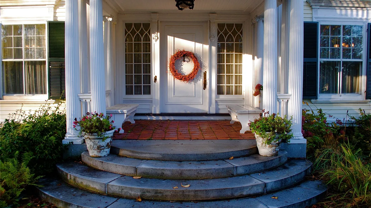 White columned front porch with curved granite steps and an autumn wreath on the door of a Maine home