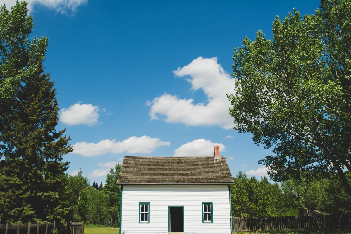 A small white farmhouse in a rural clearing surrounded by trees, for a guide to refinancing a USDA loan