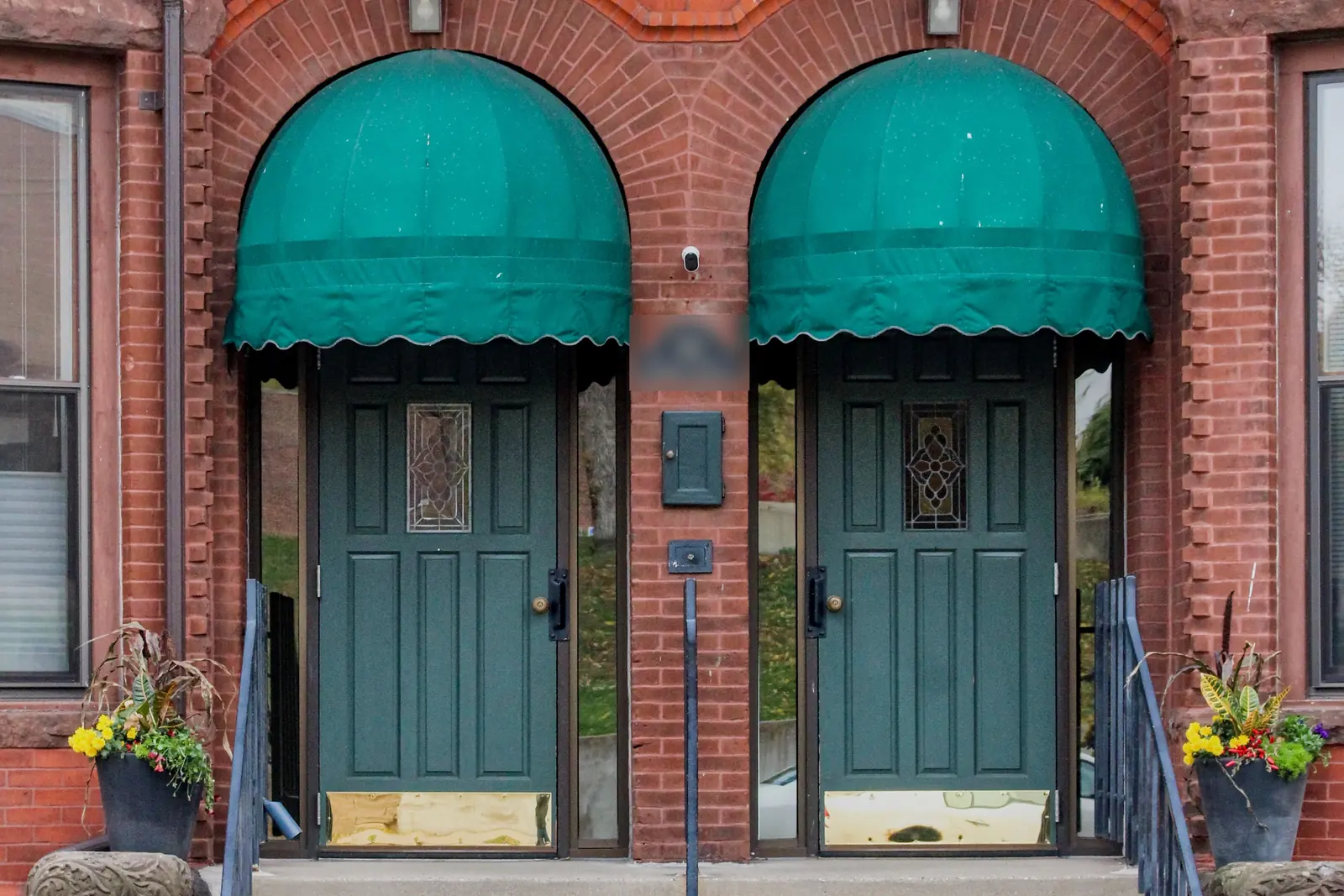 Two green front doors under matching awnings on a brick building, the kind of 2 unit rental investors buy