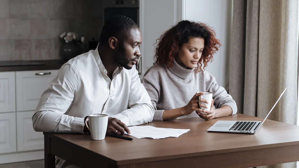A couple at a kitchen table with coffee mugs, papers and a laptop, going over their credit before a HELOC