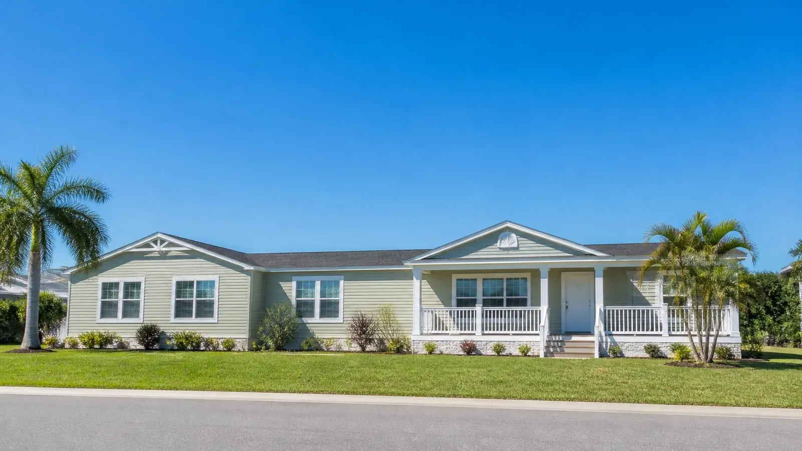 Modern double wide manufactured home with sage siding and a covered front porch in a Florida community with palm trees