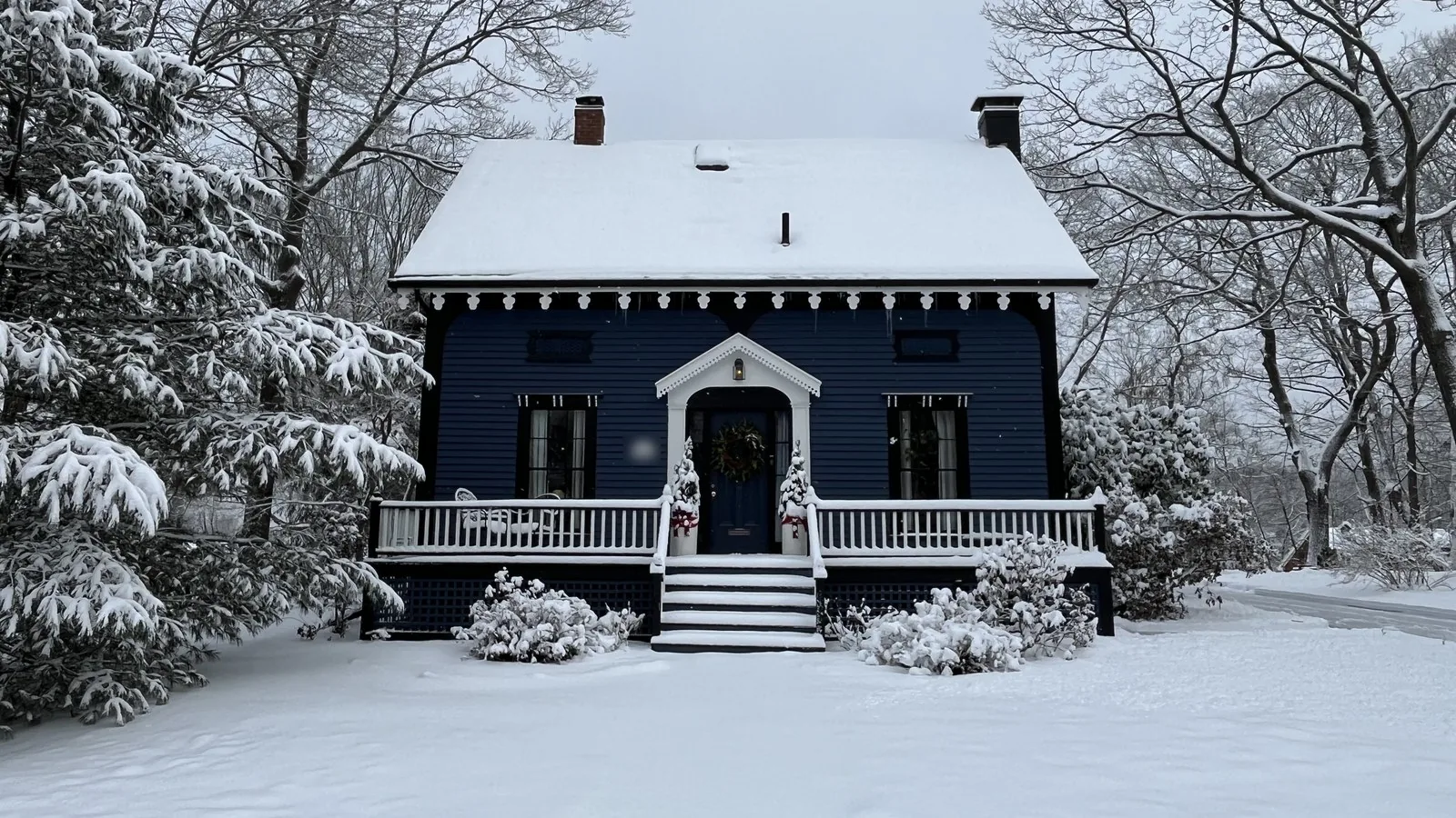 Navy blue cottage with a white front porch after a snowfall in South Portland, Maine