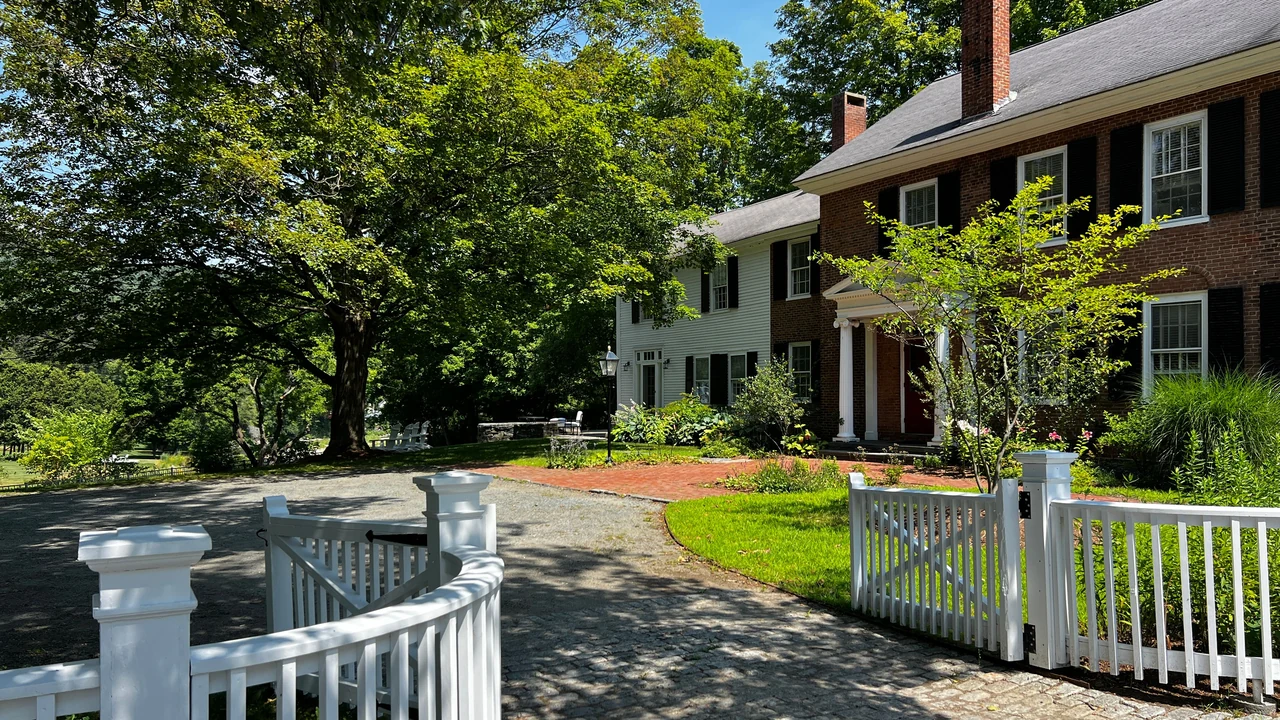 Colonial style brick and clapboard home with a white picket fence and front walk under a clear blue sky