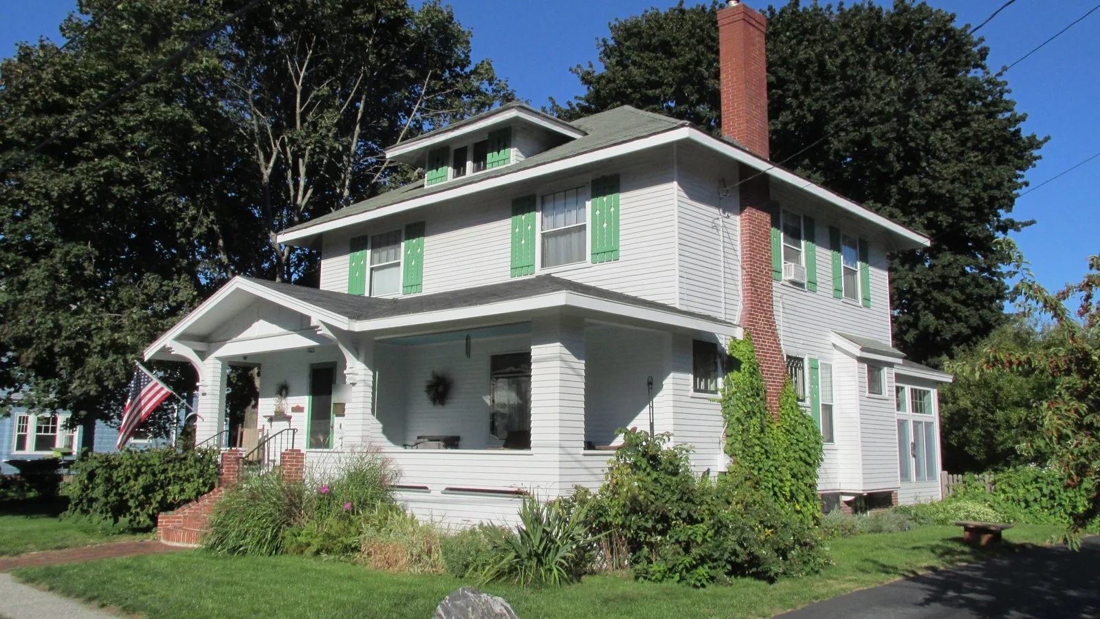 White foursquare house with green shutters and a US flag on the porch in Westbrook, Maine