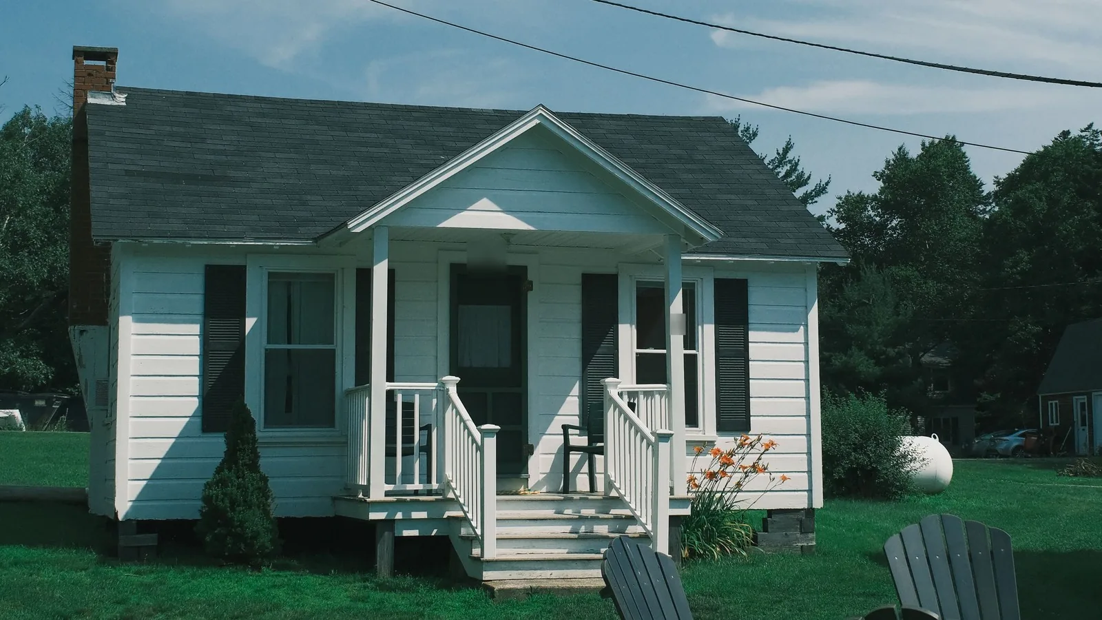 A small white clapboard cottage in Maine with a front porch and Adirondack chairs on the lawn, for a guide to finding FHA loans near you in Maine or Florida