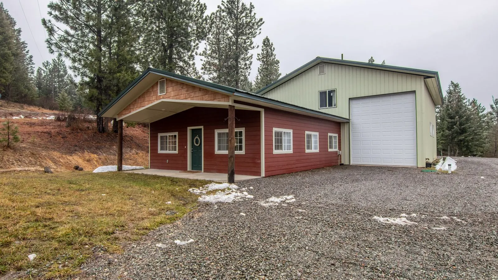 Red sided house and a big garage on a gravel drive among pines