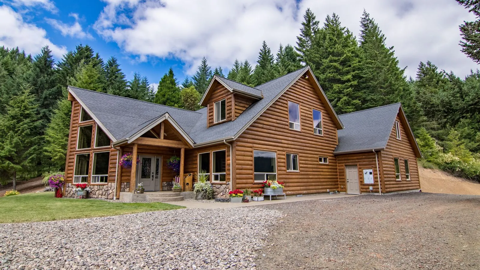 Wood sided house with a gravel drive among tall pines