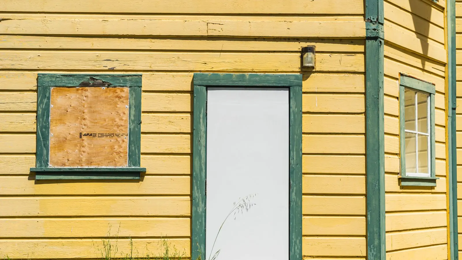 Boarded window beside the door of a yellow wooden house