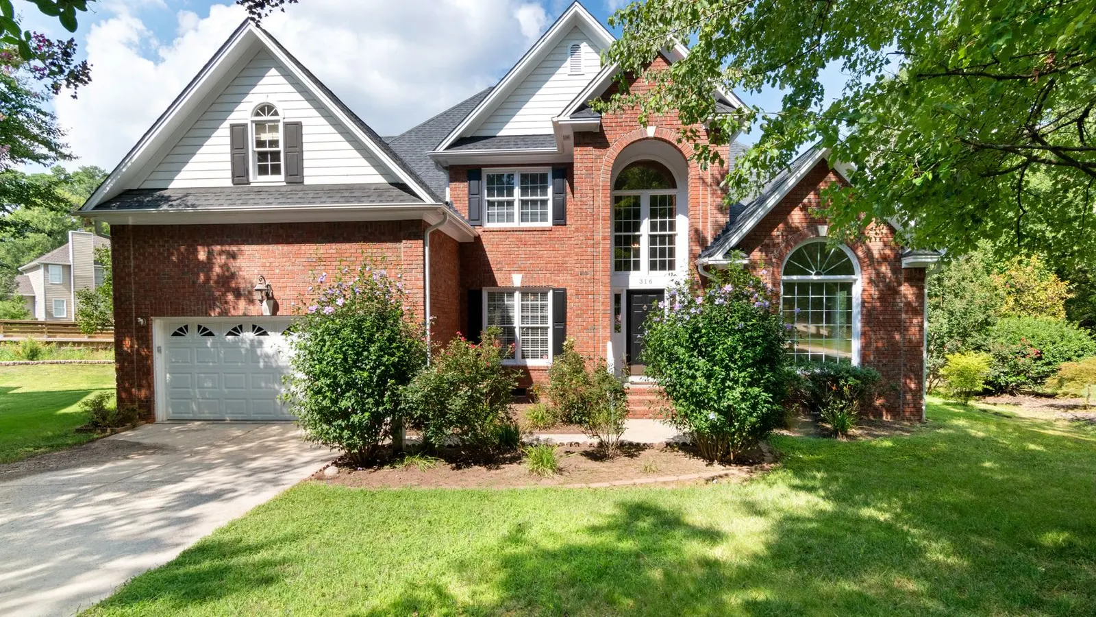 Brick house with a front gable and garage behind shrubs