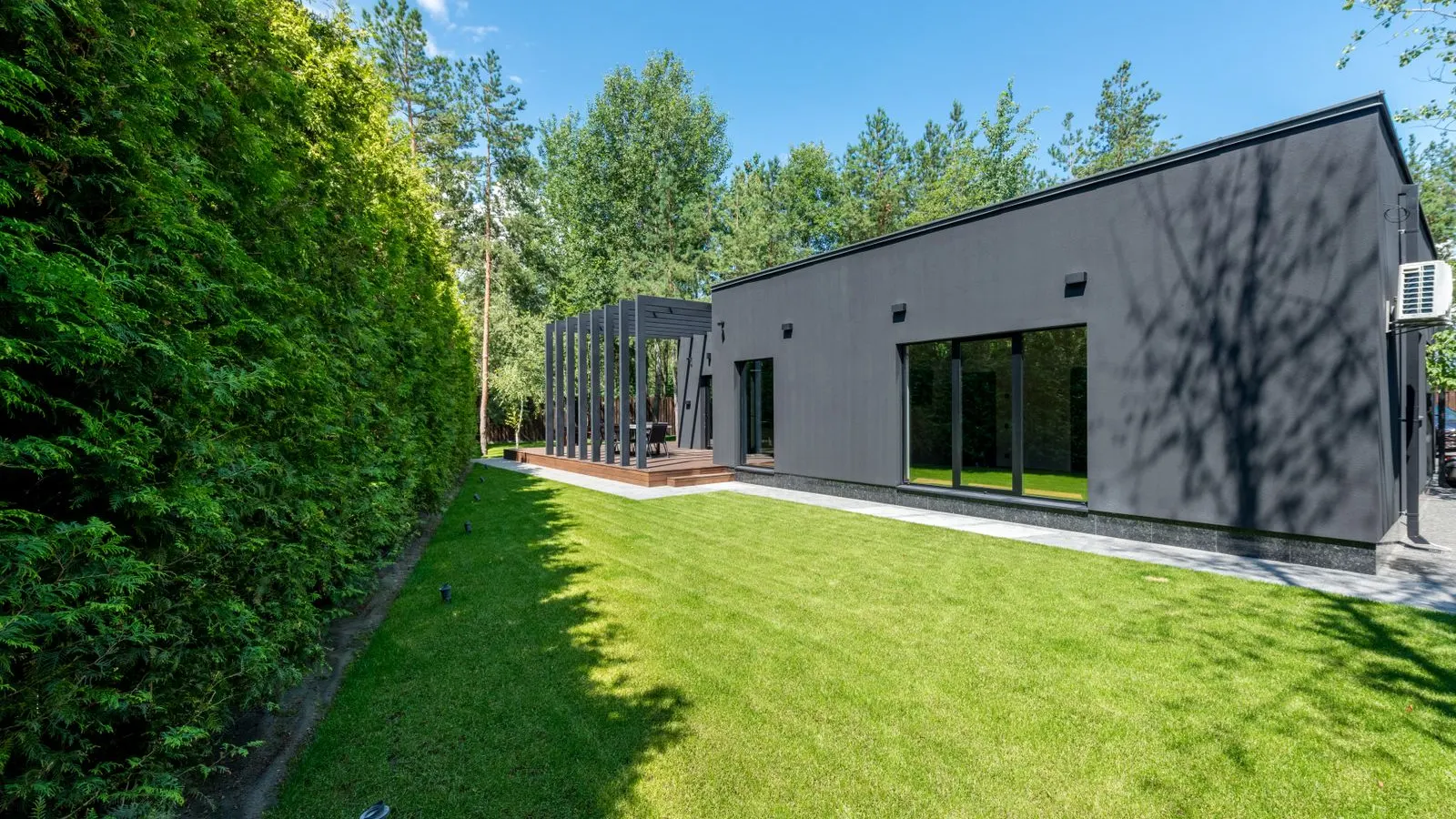 Modern dark house beside a tall hedge and lawn