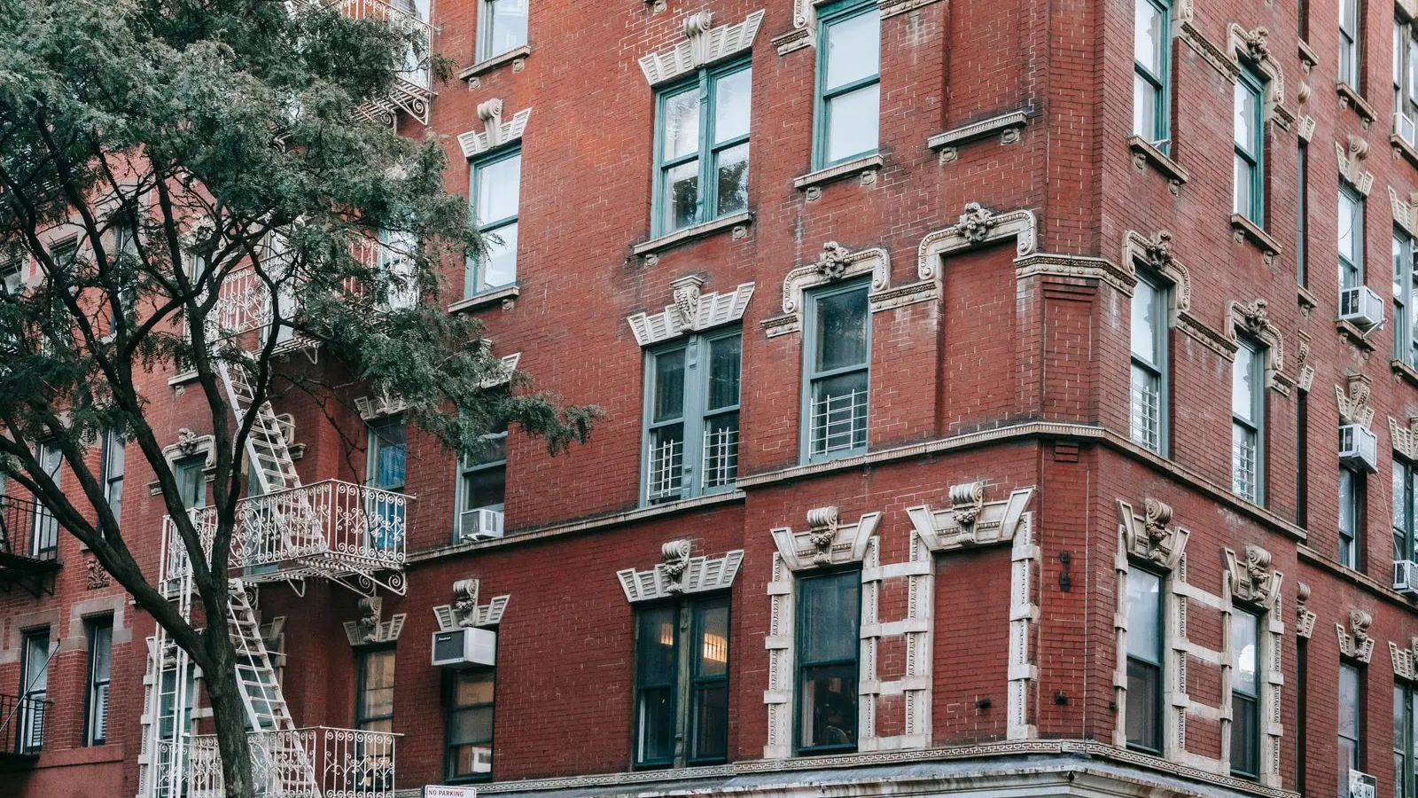 Red brick apartment building with fire escapes on a New York corner