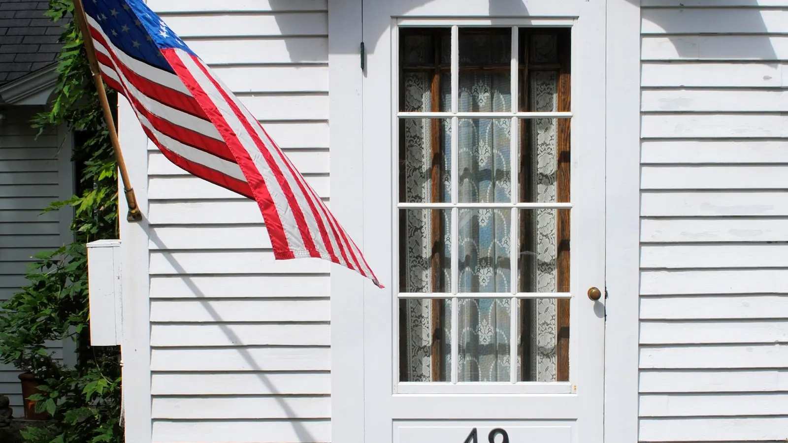 American flag beside the white front door of a house