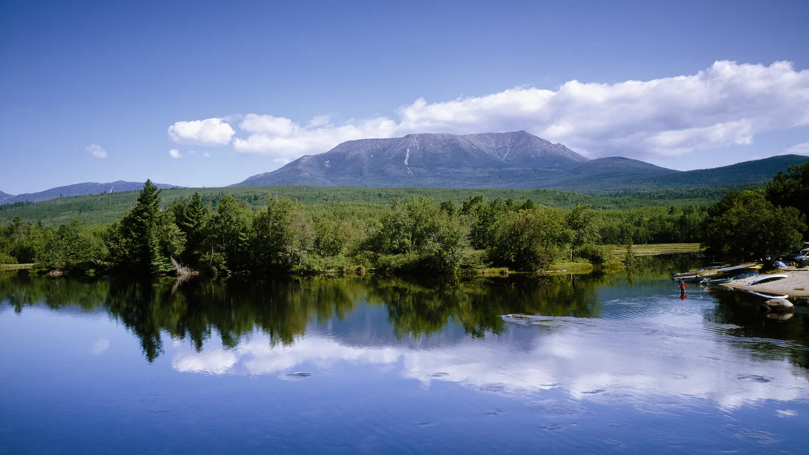 Mount Katahdin rising above a calm river and spruce forest in Maine's Katahdin region