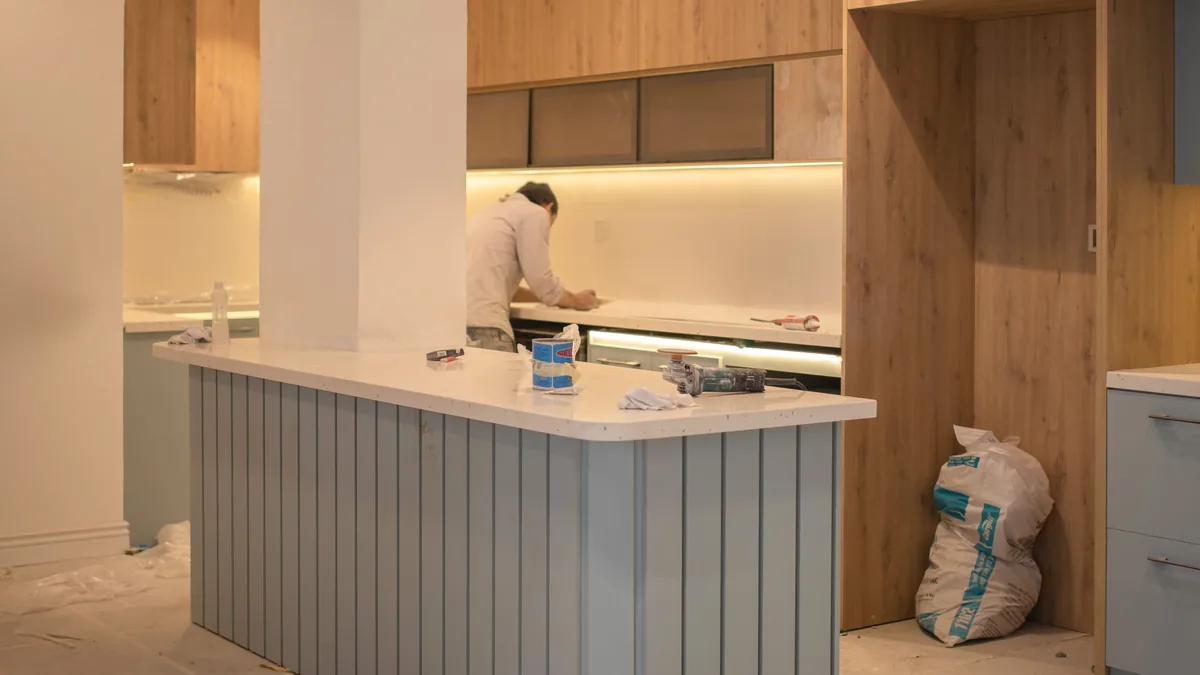 A kitchen in the middle of a renovation, with new wood cabinets, an island and paint buckets on a covered floor